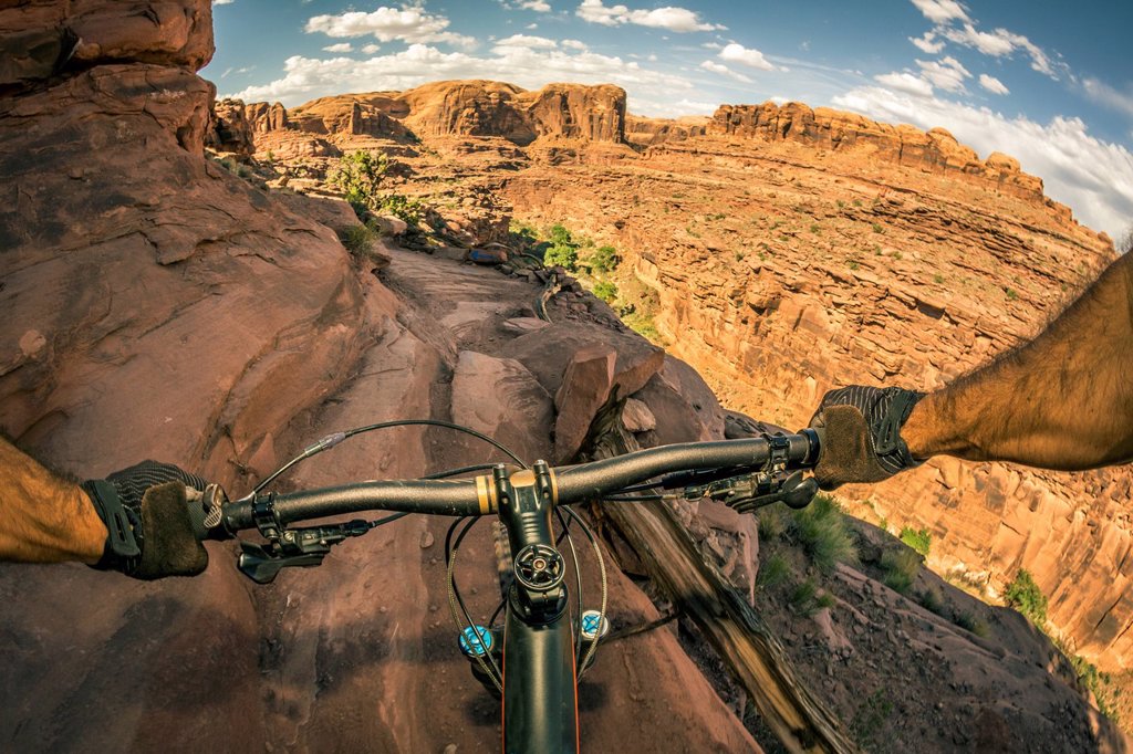 A POINT OF VIEW PERSPECTIVE OF A MOUNTAIN BIKER RIDING A TRAIL IN A RUGGED DESERT AREA.