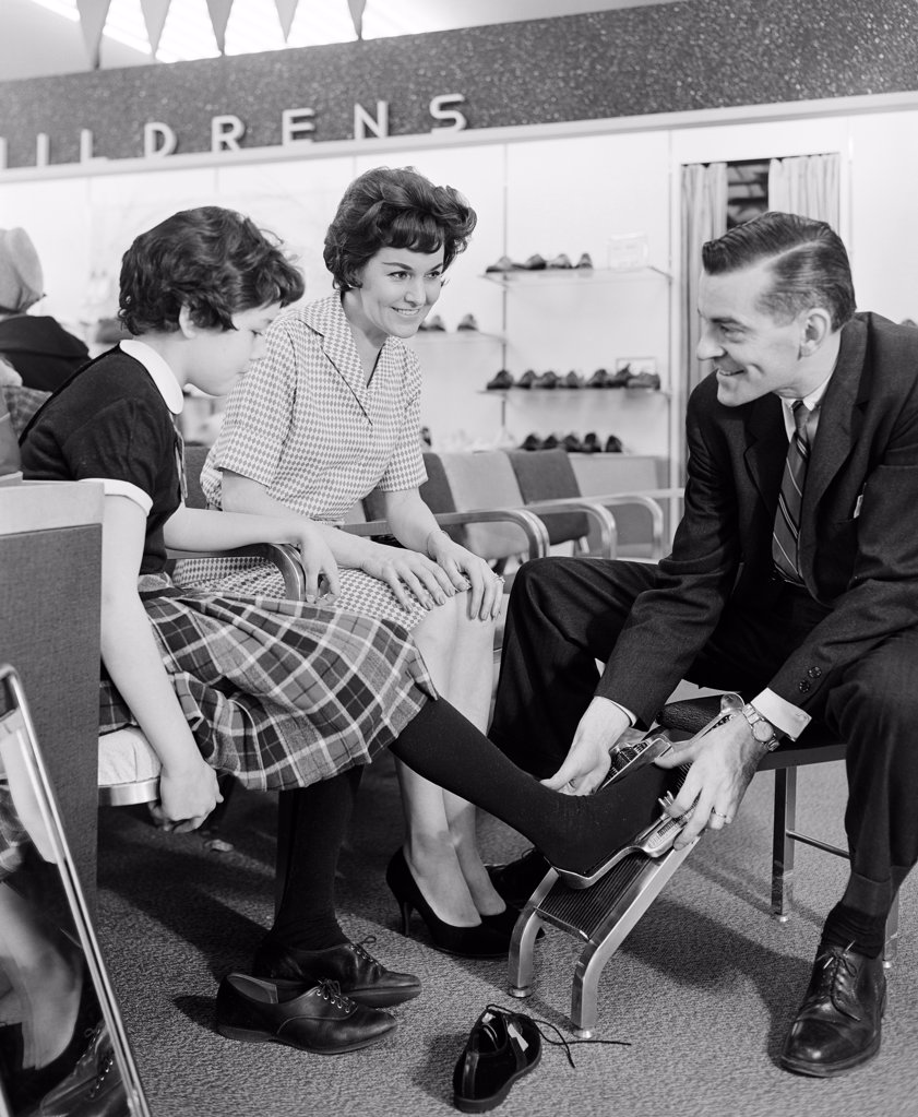 SHOP ASSISTANT MEASURING GIRLS FOOT IN SHOE SHOP