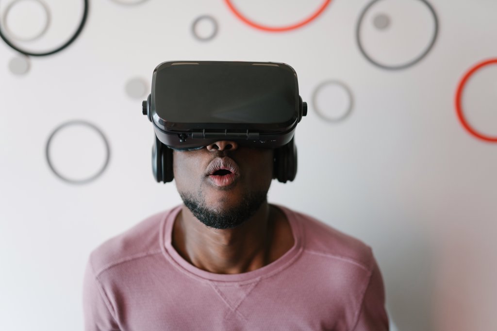 AMUSED AFRICAN AMERICAN MAN IN VR GLASSES SPENDING TIME IN VIRTUAL REALITY STAYING AT HOME