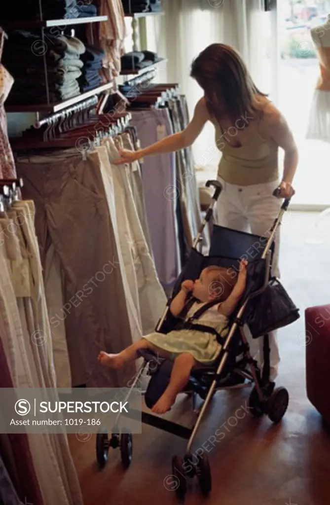 High angle view of a young woman choosing clothes in a clothing store with her daughter in a baby stroller