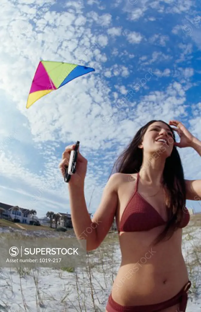 Close-up of a young woman smiling and flying a kite on the beach
