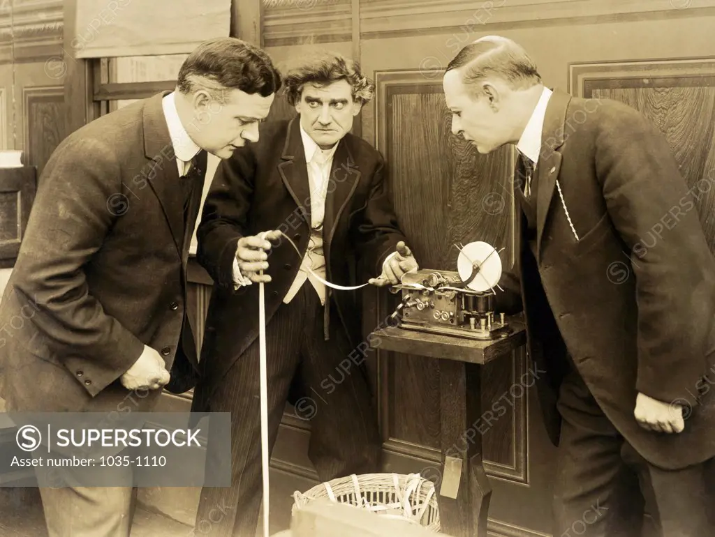 Three businessmen looking at ticker tape