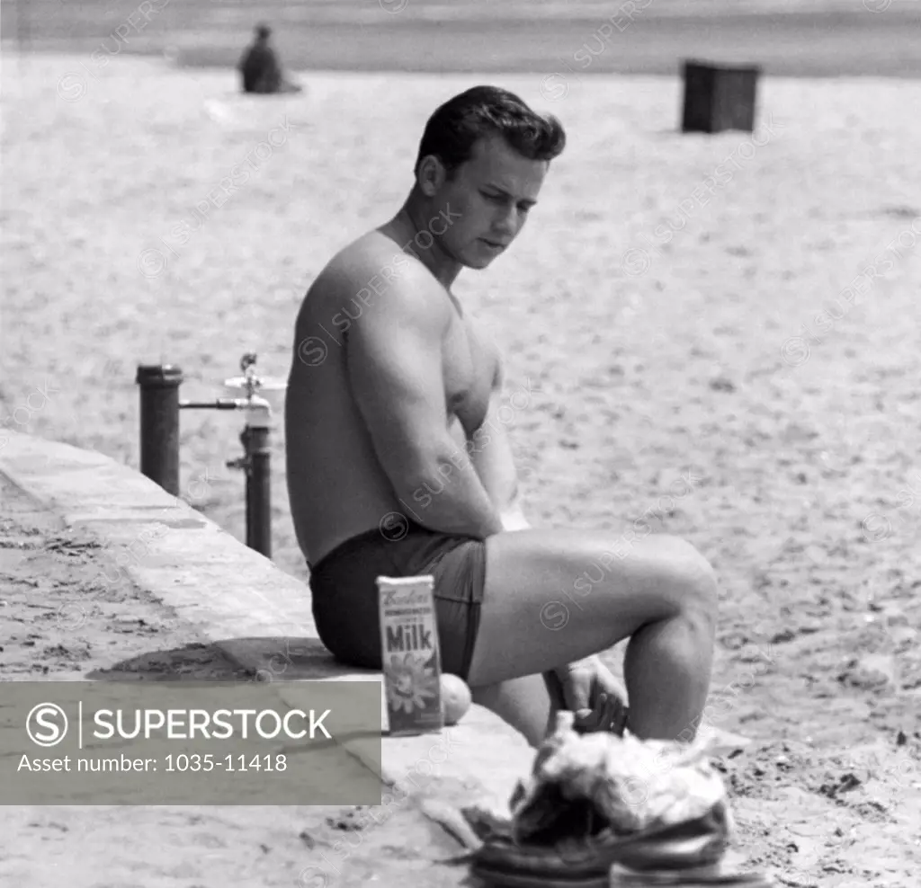 San Francisco, California: c. 1953. A well muscled man on the beach contemplates his quart of Bordens milk.©Underwood Archives