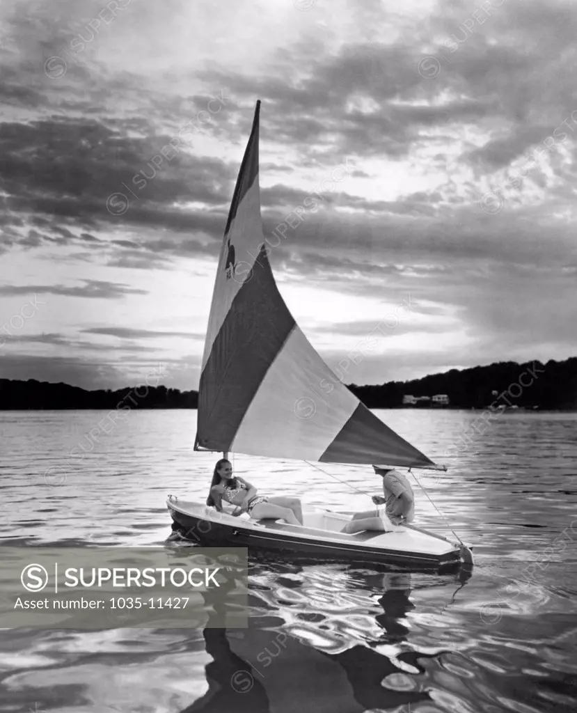 United States: 1975. A couple enjoy a tranquil sunset sail in their Silverline Dolphin Senior sailboat.©Underwood Archives