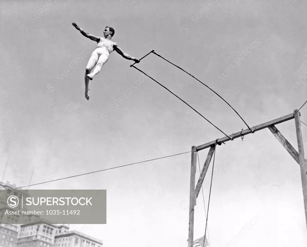 United States:  c. 1933. Alfredo Codona, trapeze artist, at the apex of his swing on the trapeze.