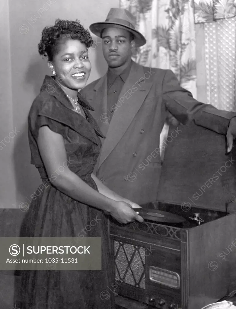 United States:  c. 1940. A stylish African American couple playing 78 rpm records on a record player.