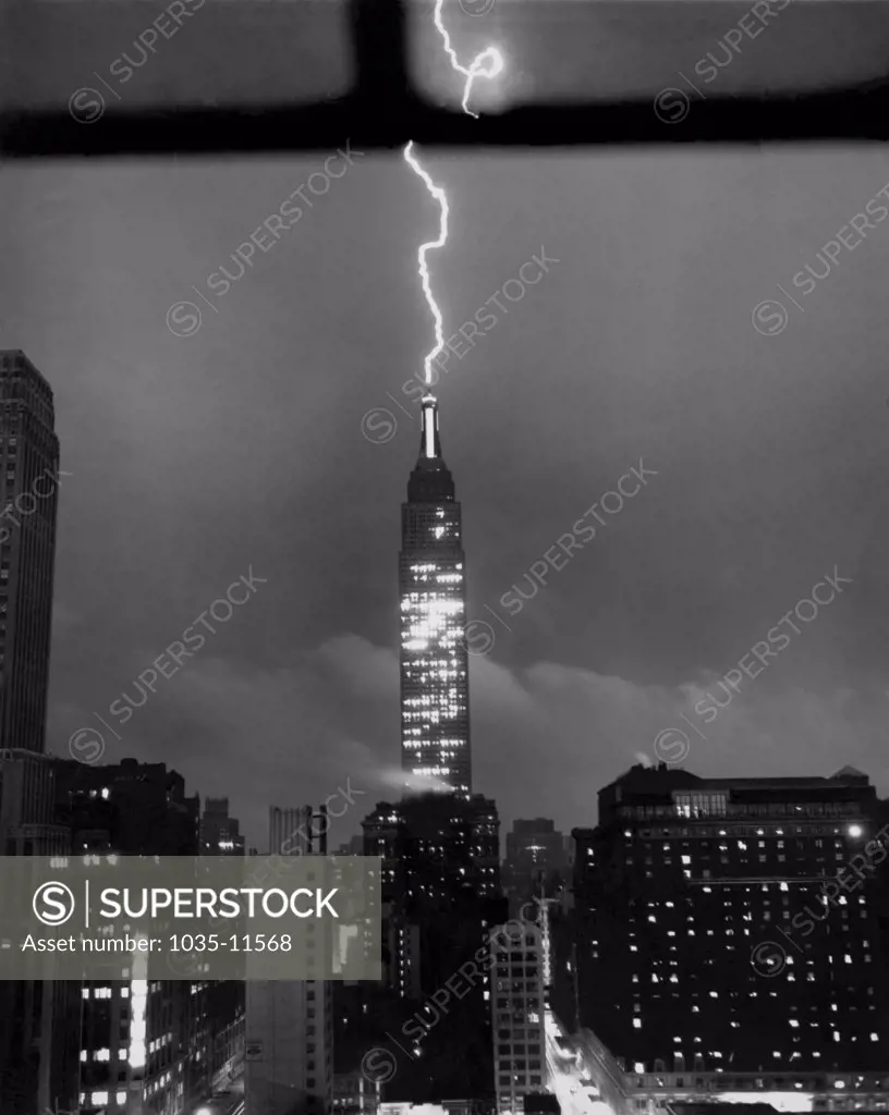 New York, New York:  July 9, 1945. As the city is hit by a sudden summer storm, a jagged streak of lightning crackles down through  the sky to roost on the tip of the dome of New York's Empire State Building high above Manhattan's streets.