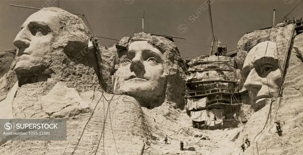 Mt. Rushmore, South Dakota:  c. 1938. Workmen on the faces of Mount Rushmore.  Roosevelt has the scaffolding over his face.