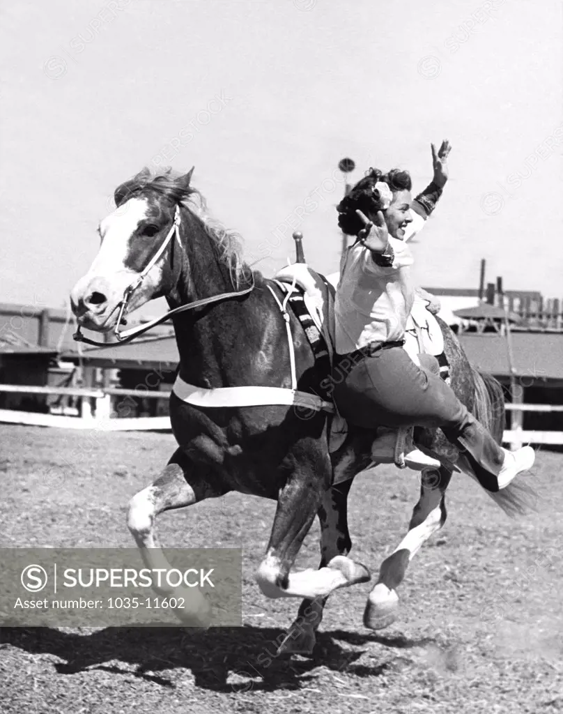 Los Angeles, California:  c. 1947. A cowgirl shows off her stunt riding skills with only one foot attached to the horse.