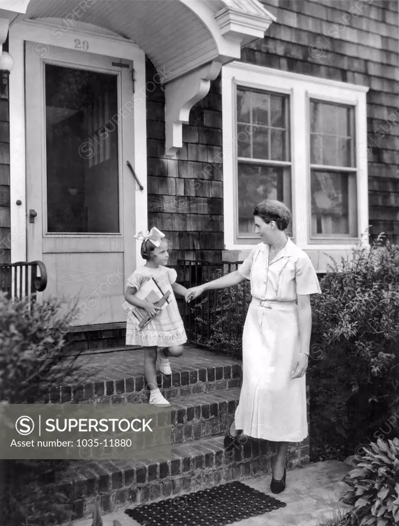 United States:  c. 1930. A mother takes her daughter by the hand on the way to the first day of school.