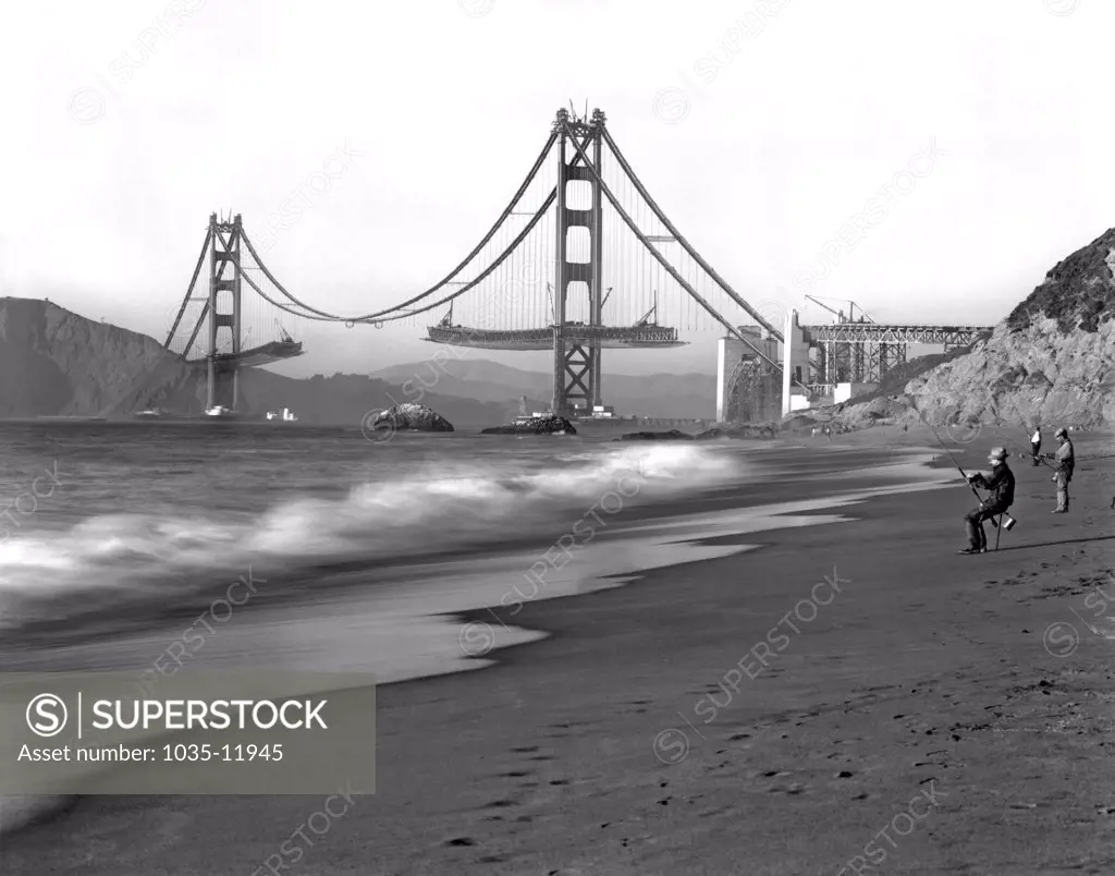 San Francisco, California:   c.1936. Fishermen on Baker Beach enjoy the view of the Golden Gate Bridge under construction.