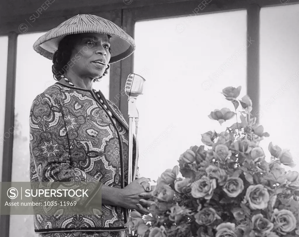 United States: c. 1940. Marian Anderson wearing a hat speaking at a microphone.