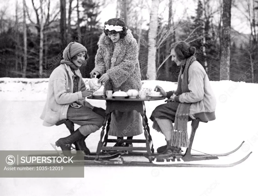 Lake Placid, New York:  January 3, 1923. Two young women ice skaters at the Lake Placid Club enjoy an afternoon tea served hot off the ski-tea table.