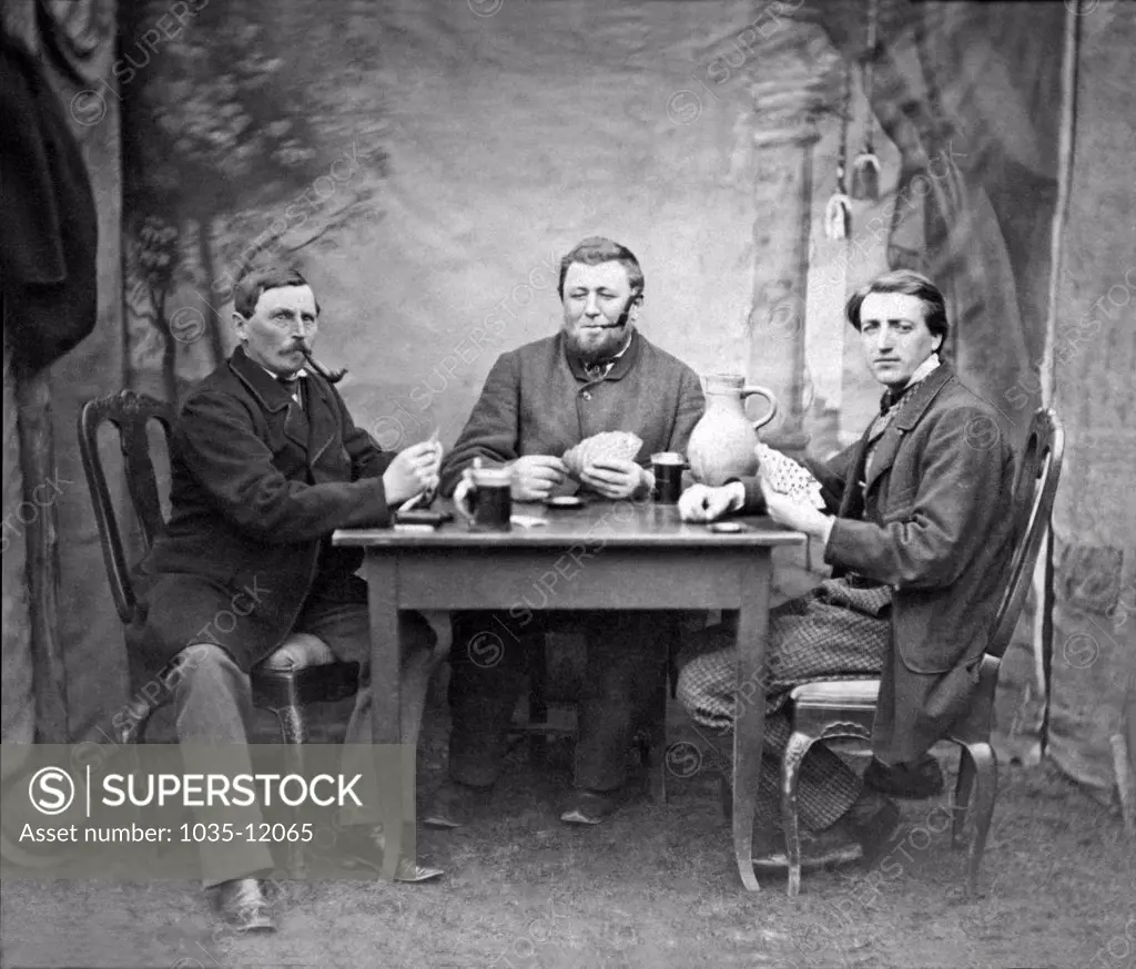 United States:  c. 1885. Three men drinking, smoking, and playing cards at a table.