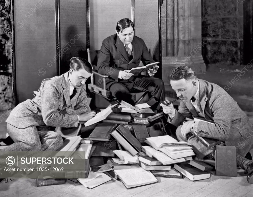 Hollywood, California:  c. 1927. Ernst Lubitsch (1898-1947) at the center with two other men searching through a large pile of books.