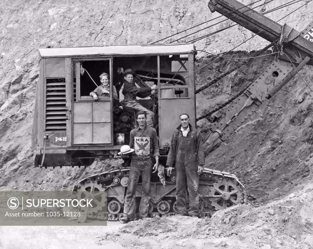 United States:  c. 1935. A couple of kids pretend to run the steam shovel at a mine while the fathers stand by. One is wearing an NRA (National Recovery Act) sign on his chest.