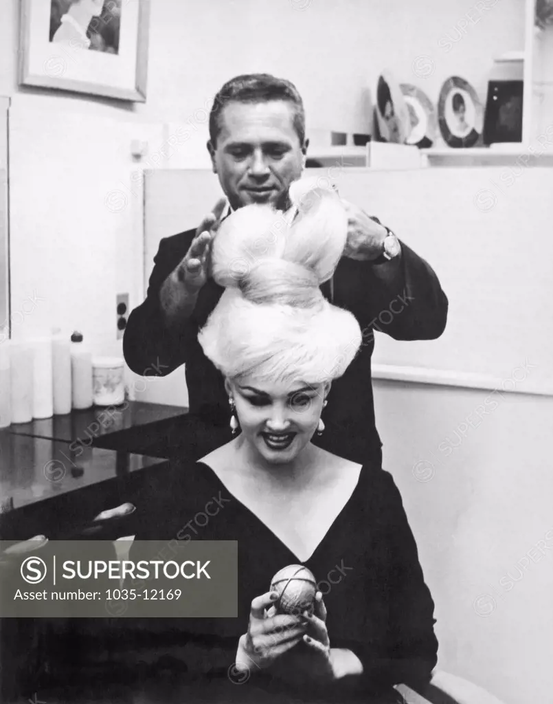New York, New York:  1964. Stylist John Fonda puts the finishing touches on 'The Unisphere Hairdo', on Ecstasy, a featured stripper in the Broadway play, 'This Was Burlesque'. The hair was inspired by the official symbol of the 1964 NY World's Fair.
