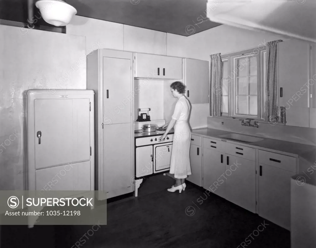 Beaver Dam, Wisconsin  c. 1932. A woman cooking in her sparsely furnished kitchen.
