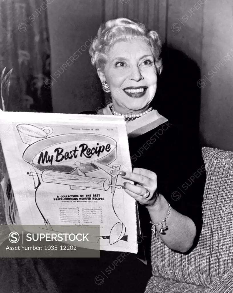 United States:  c. 1958.  A woman reading a newspaper tabloid titled 'My Best Recipe'