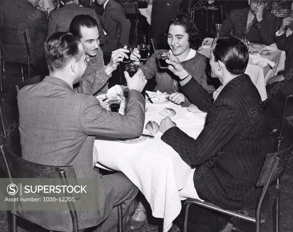 New York, New York:  c. 1939. Four friends share a toast at a dinner in a restaurant.