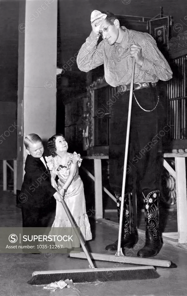 United States:  c. 1938. Robert Wadlow, the world's tallest man, share sweeping duties with two members of the Doll family  while on tour with the Ringling Brothers/Barnum & Bailey Circus.