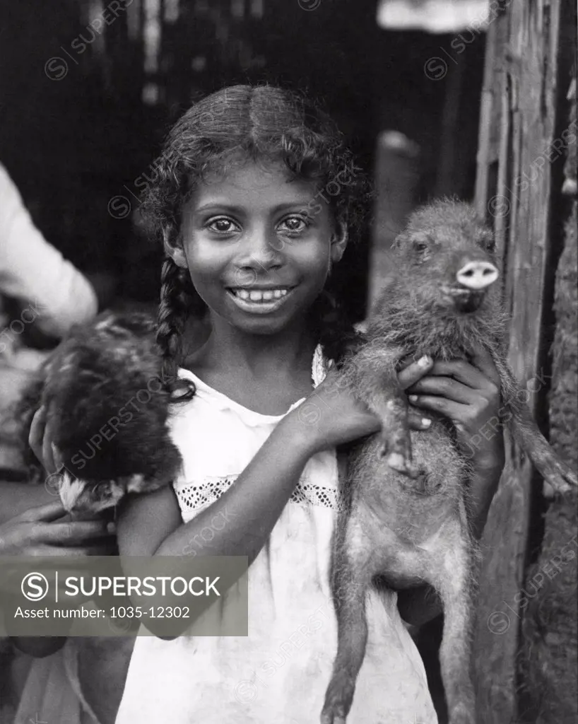 Panama:  c. 1935. A young girl from Panama holding her pet baby peccary.