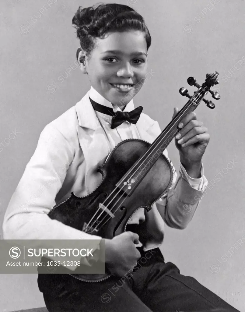 California: c. 1929. A smiling young African American girl dressed in a tux and bow tie proudly holds her violin.