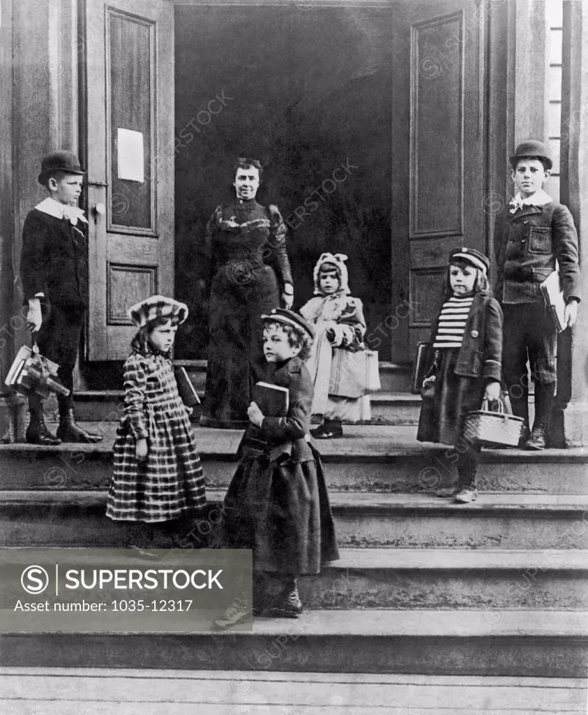 United States:  c. 1880. Children arriving at school with their books straps and wicker lunch baskets.