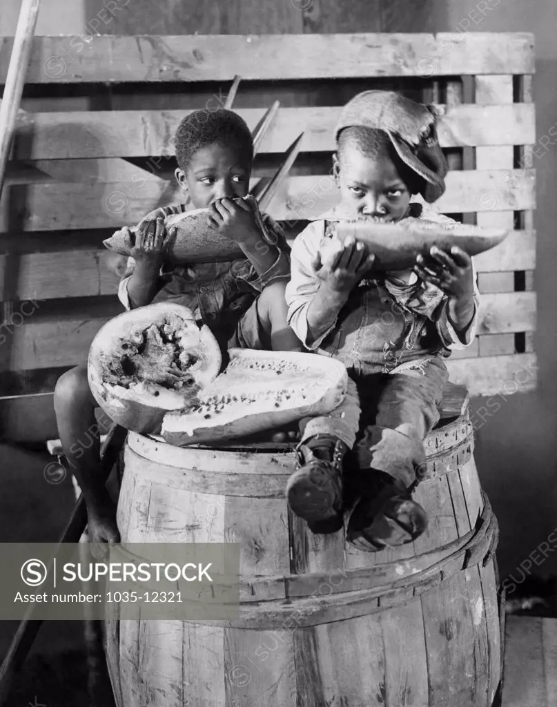 New York, New York:  November 8, 1924 Two young African American boys sitting on a barrel dig into a watermelon. The original 1924 press caption read: 'A Thanksgiving Feast In Darky Town'.