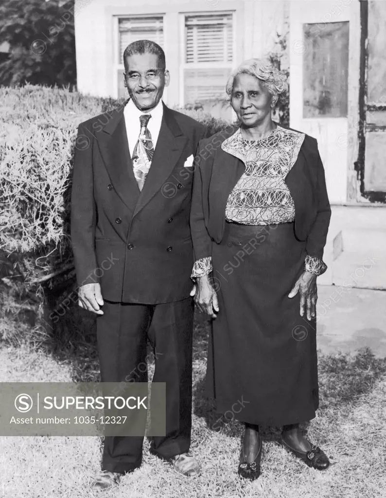 United States:  c. 1938 An older African American man and his wife pose for a portrait outside their home.