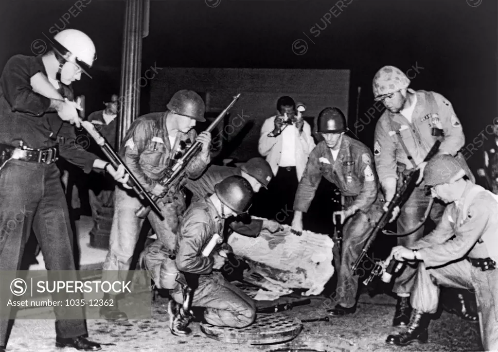 Los Angeles, California,  August 18, 1965.    A heavily-armed group of police and National Guardsmen stand ready at an open manhole after dropping a tear gas shell inside. Shooting suspects were believed to be using the storm sewer system to escape capture after a gun battle between the police and Black Muslims.