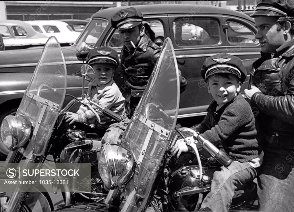 San Francisco, California  c. 1954 Two bikers wearing caps and leather jackets on their Harley Davidsons with their small sons in front of them. The boys are wearing caps that say 'Harley Davidson Motor Cycle'.