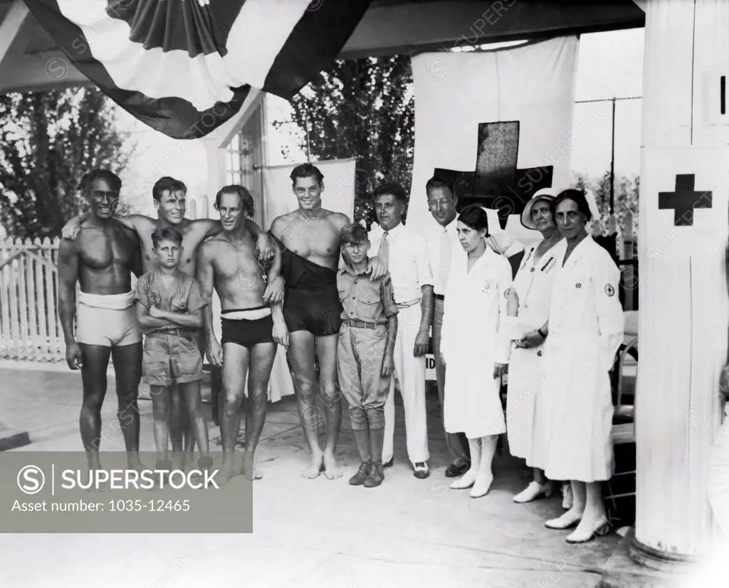 Cincinnati, Ohio:  July, 1932 At the Olympic tryouts are,left to right: Duke F. Kahanamoku, Clarence 'Buster' Crabbe, Harold 'Stubby' Kruger, Johnny Weissmueler, Judge Elmer F. Hunsicker, Paul Goss, Mrs. Mabel Fitzmorris, Mrs. Ella Layne Brown, and Mrs. Carolyn Wayman. Two boy scout messengers stand in front.