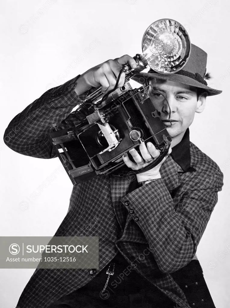 United States:   1936 A press photographer aims his flash camera.