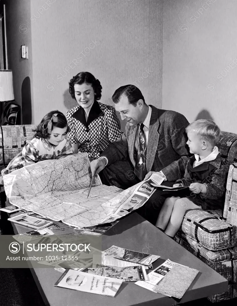 United States:  1951 A family of four plan their summer travel with maps and brochures.