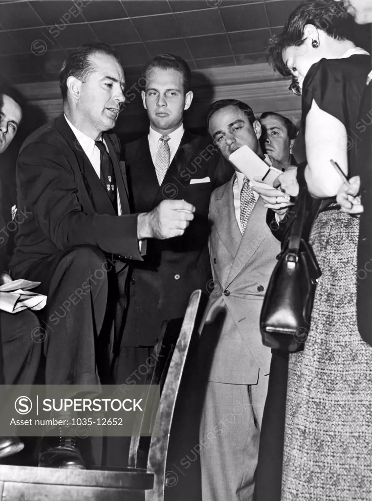 New York, New York:  1953    Senator Joseph R. McCarthy (left), discusses the State Department's Voice of America program with newsreporters in New York, while associates David Schine (center) and Roy Cohn (right) stand by.