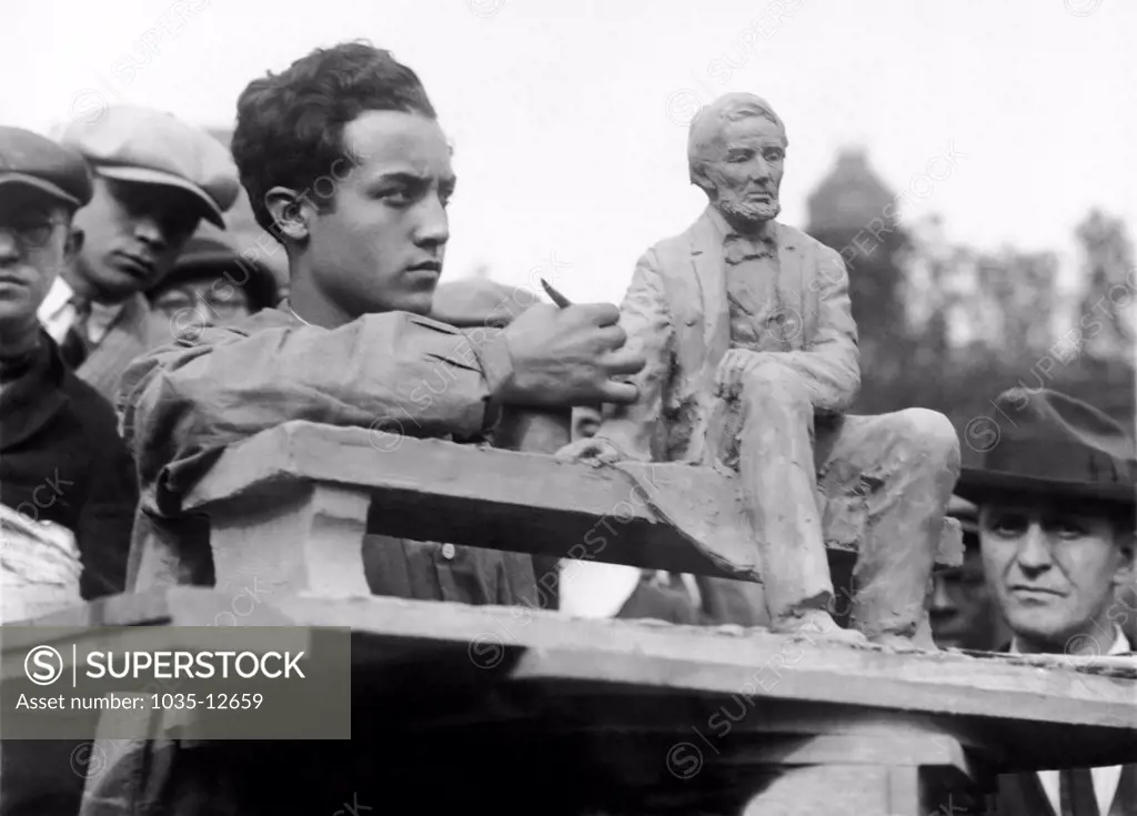 Newark, New Jersey:  November 11, 1924 Isamu Noguchi, 19 year old star pupil of the New Leonardo da Vince Art School in New York. Here he is modeling a miniature copy of the Lincoln Monument while passersby look on in wonder and admiration.