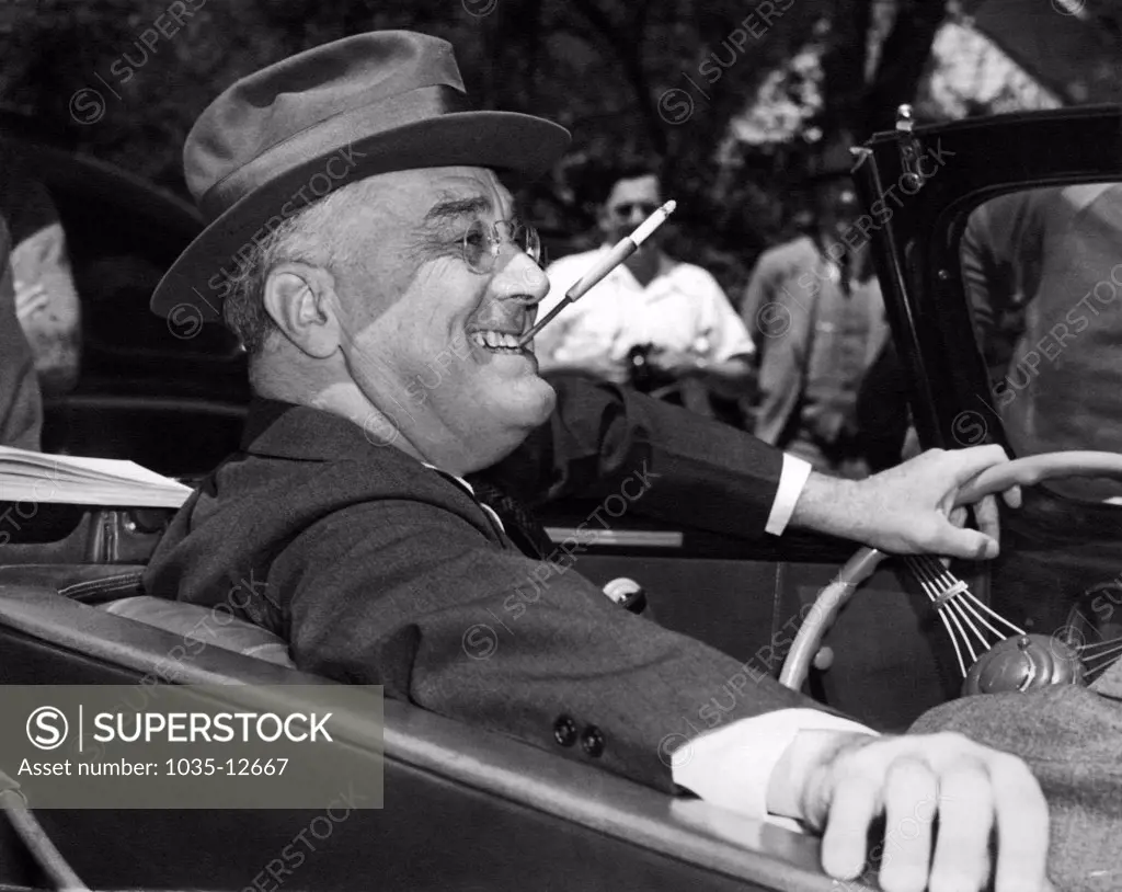 Warm Springs, Georgia:  1939. With a cigarette in a holder clenched in his teeth, a smiling Franklin Delano Roosevelt sits jauntily at the wheel of his convertible.