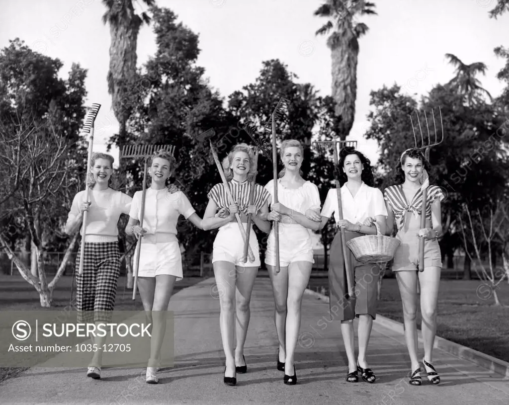 United States:  c. 1960 Six women walking on a pathway carrying gardening tools.