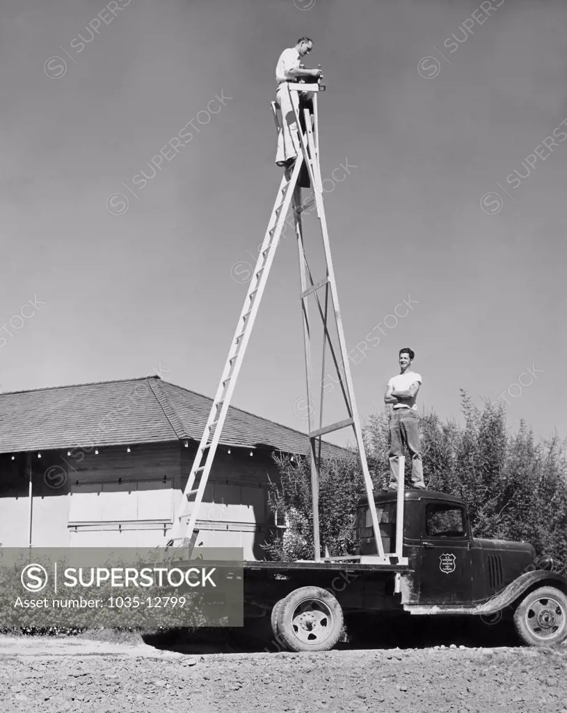 United States:  c. 1931 A U.S. Department of Agriculture photographer gets up high on a ladder for a photograph of the surrounding landscape.