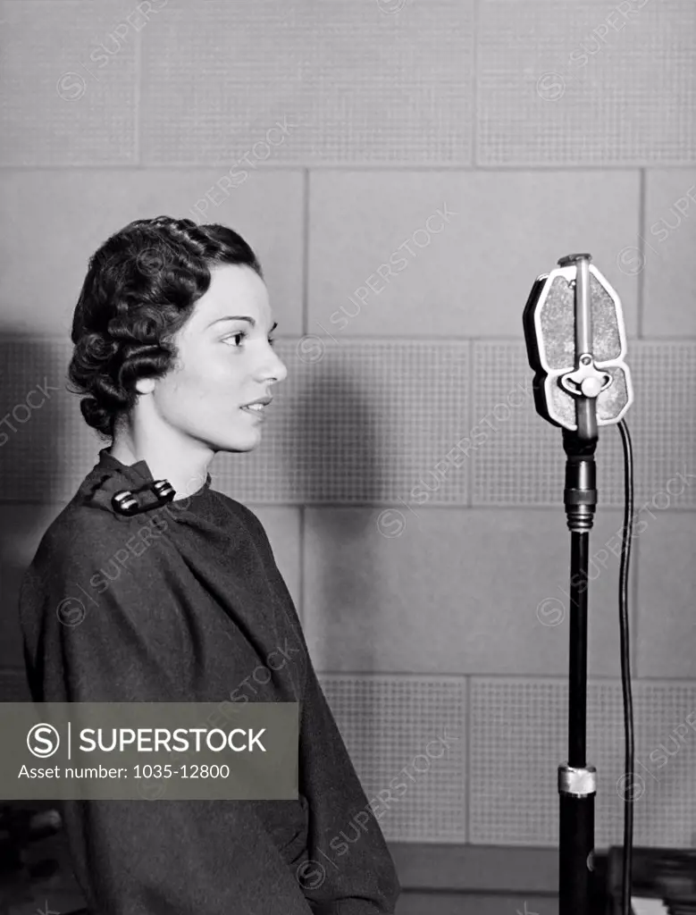 New York, New York:  c. 1937 A woman stands in the WOV studio in front of the microphone.