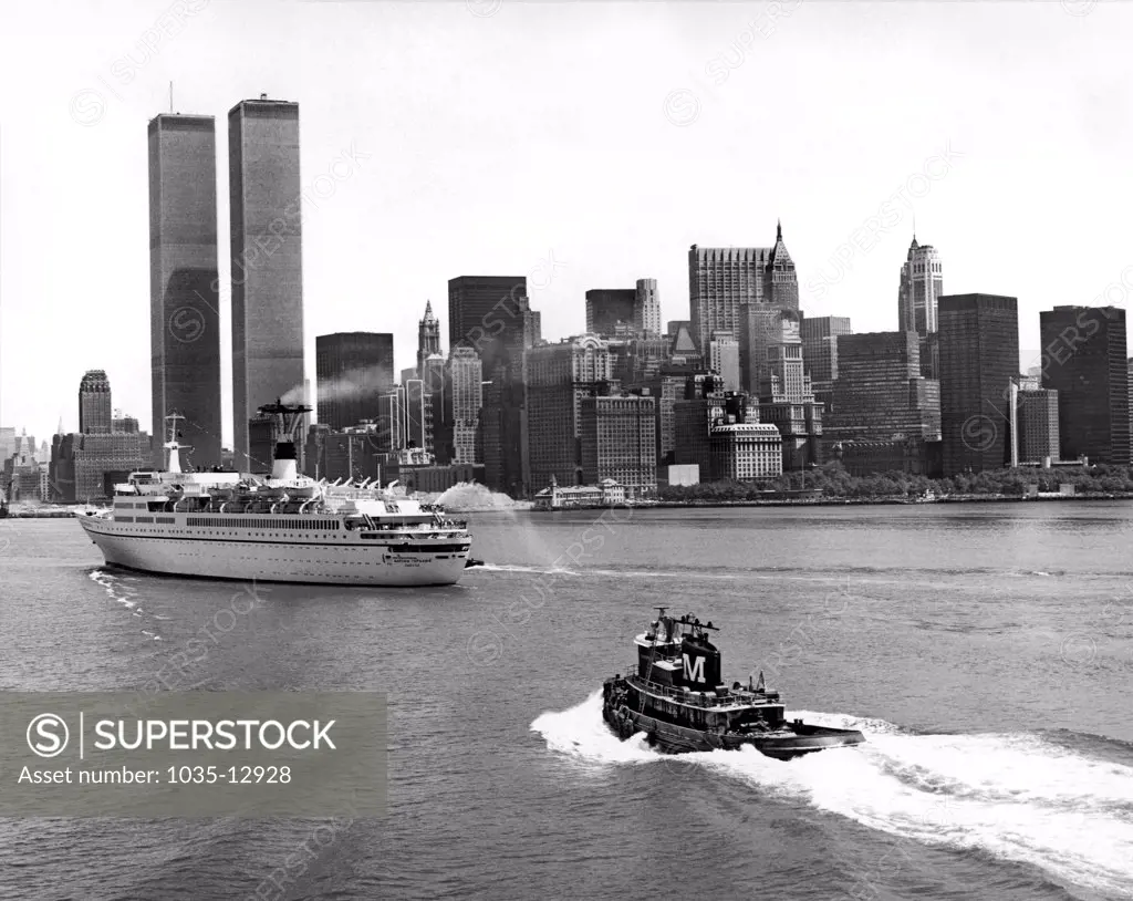 New York, New York:  c. 1975 A Moran tugboat trails a cruise ship up the Hudson River towards the World Trade Center twin towers in New York City.