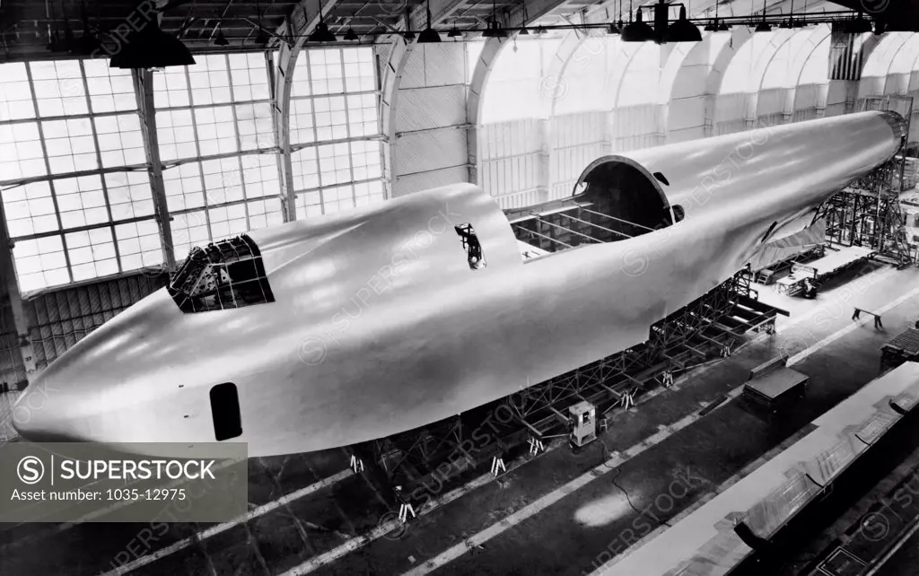 Culver City, California:    c. 1946 The 220 foot long hull of Howard Hughes' flying boat under construction in its hangar. It is near completion with its final coat of aluminum lacquer. The cut away section is where the wings will fit together.