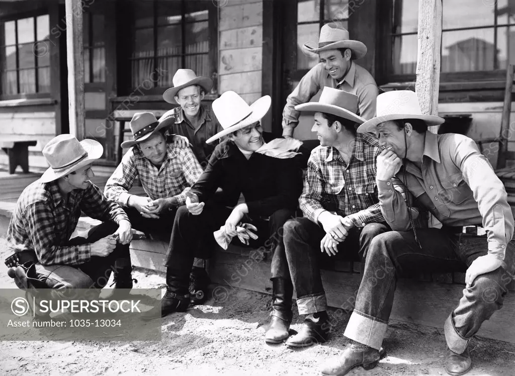 Hollywood, California:  c. 1925 Cowboy actor Tom Mix sitting and chatting on a porch with a group of cowboys.