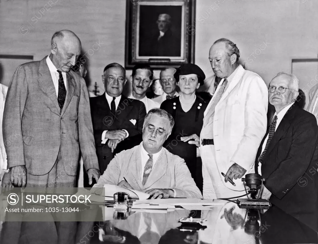 Washington, D.C.:  1935  President Franklin D. Roosevelt signs the Social Security Bill. Standing behind Roosevelt, left to right are: Rep. Robert Doughton, Senator Robert Wagner, Secretary of Labor Frances Perkins, Senator Pat Harrison, Rep. David J. Lew