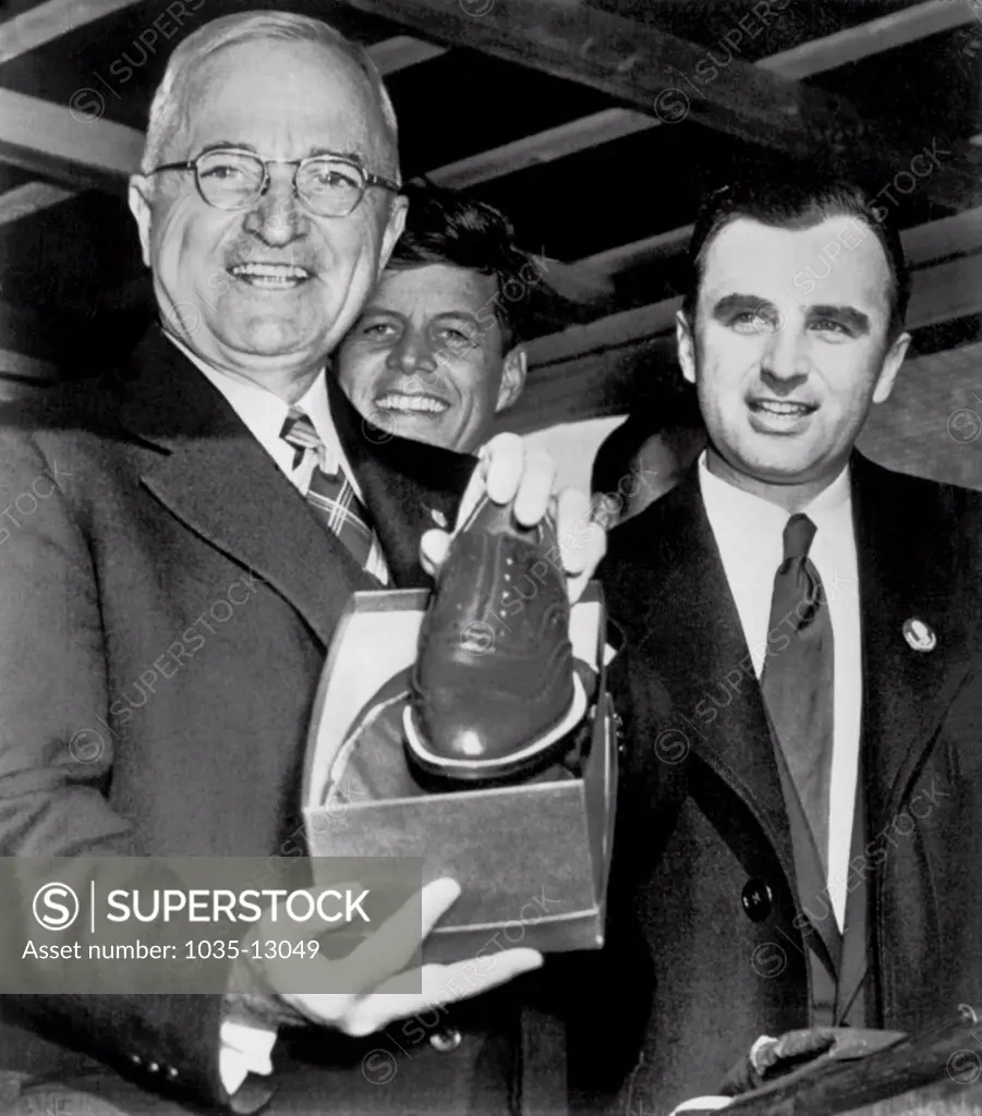 Brockton, Massachusetts:  October 18, 1952 President Truman displays a pair of shoes presented to him by Mayor Lucey (r) in this shoe center as the President continued his whistle stop tour of New England in his campaign for Democratic candidate Adlai Stevenson.  John F. Kennedy, who was not noted in the press release, stands in the background.