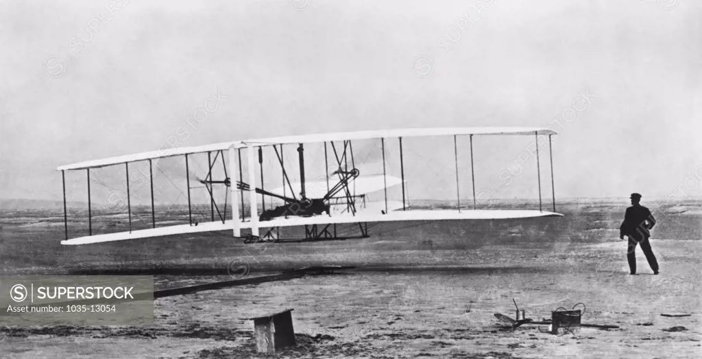 Kitty Hawk, North Carolina:  December 17, 1903 Orville Wright flying during the first powered and sustained flight while Wilbur is on the ground at right.
