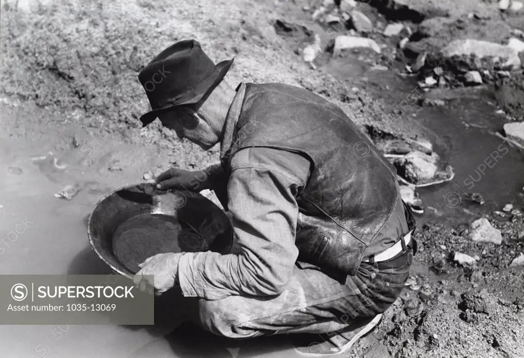 Pinos Altos, New Mexico:  May, 1940  A prospector panning for gold. The light objects in his pan are probably not gold as it is very unusual to find pieces this large in this section. They are probably mica (fools' gold) or mercury, which is used to attract the gold