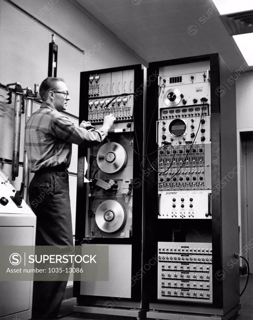 United States:  c. 1970 A man working with a Sangamo analog 1 inch tape recorder that can take down 14 channels of simultaneous information.