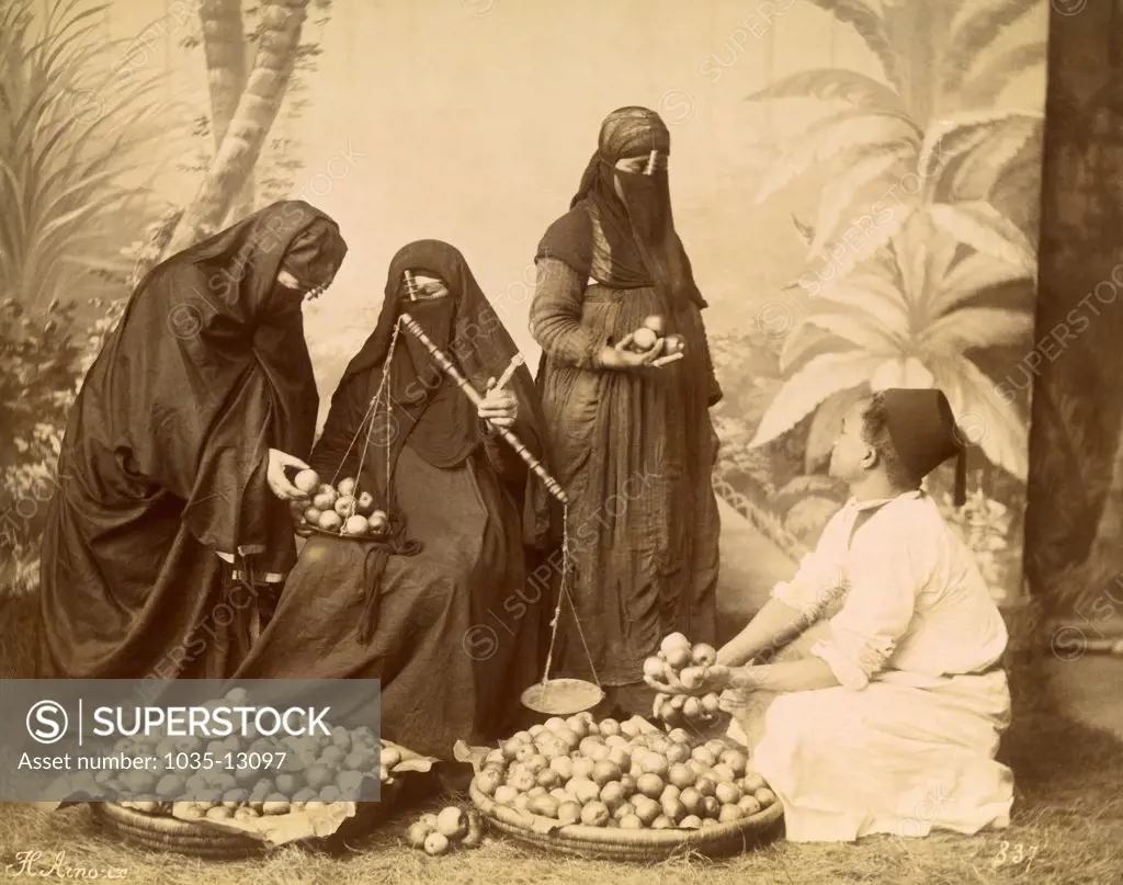 MIddle East:   c. 1890 An albumen print of three Arab women using a scale to buy fruit from a vendor.